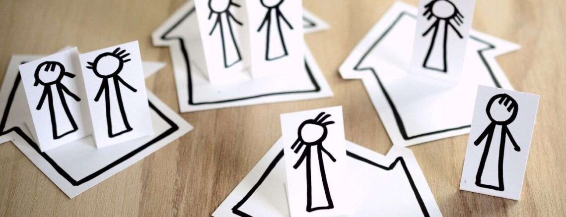 Cutouts of stick people placed on cutouts of houses which are arranged on a table