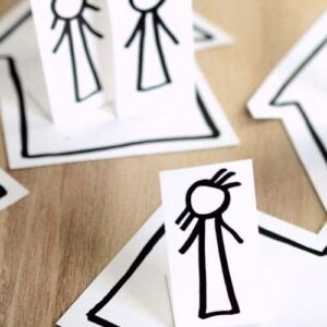 Cutouts of stick people placed on cutouts of houses which are arranged on a table