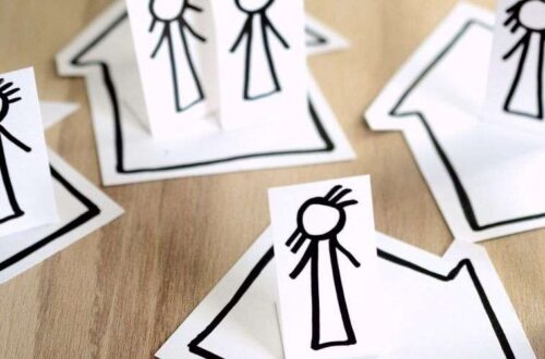 Cutouts of stick people placed on cutouts of houses which are arranged on a table